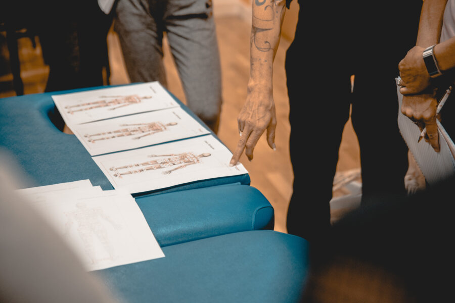 Photo of a skeleton and diagram with circles around certain points. Rcahel is pointing to the paper, and the paper is sat on a massage table.