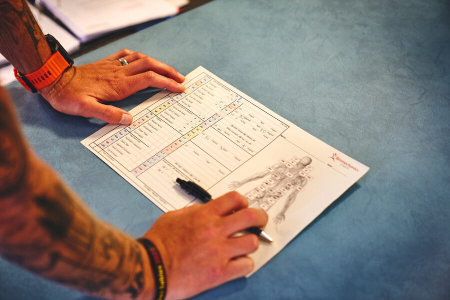 PHOTO OF HANDS ON A SHEET OF PAPER, WITH A DIAGRMA OF THE BODY AND MAKRING OUT AREAS OF BIOMECHANICS